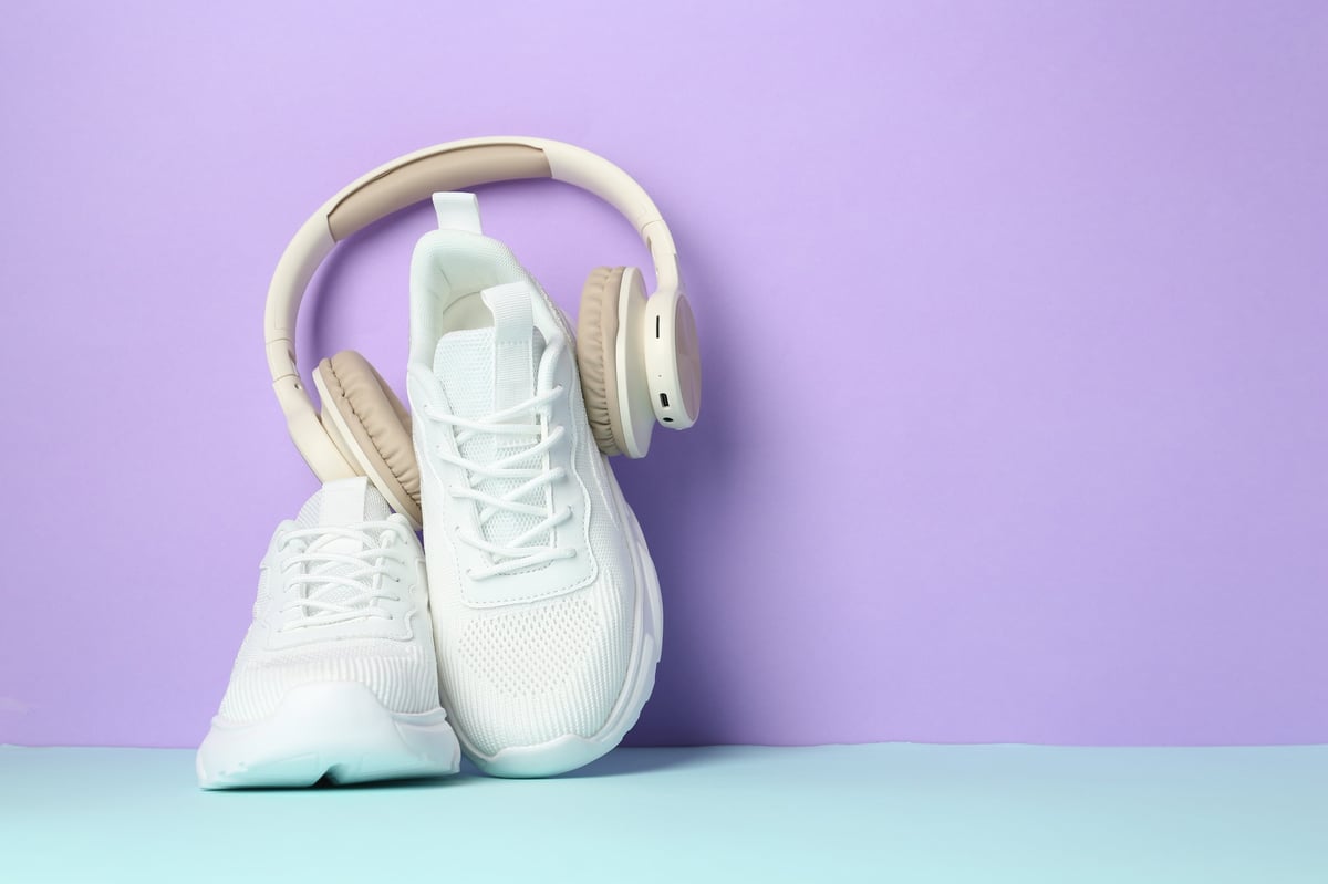 Pair of white sneakers with headphones on a colour background