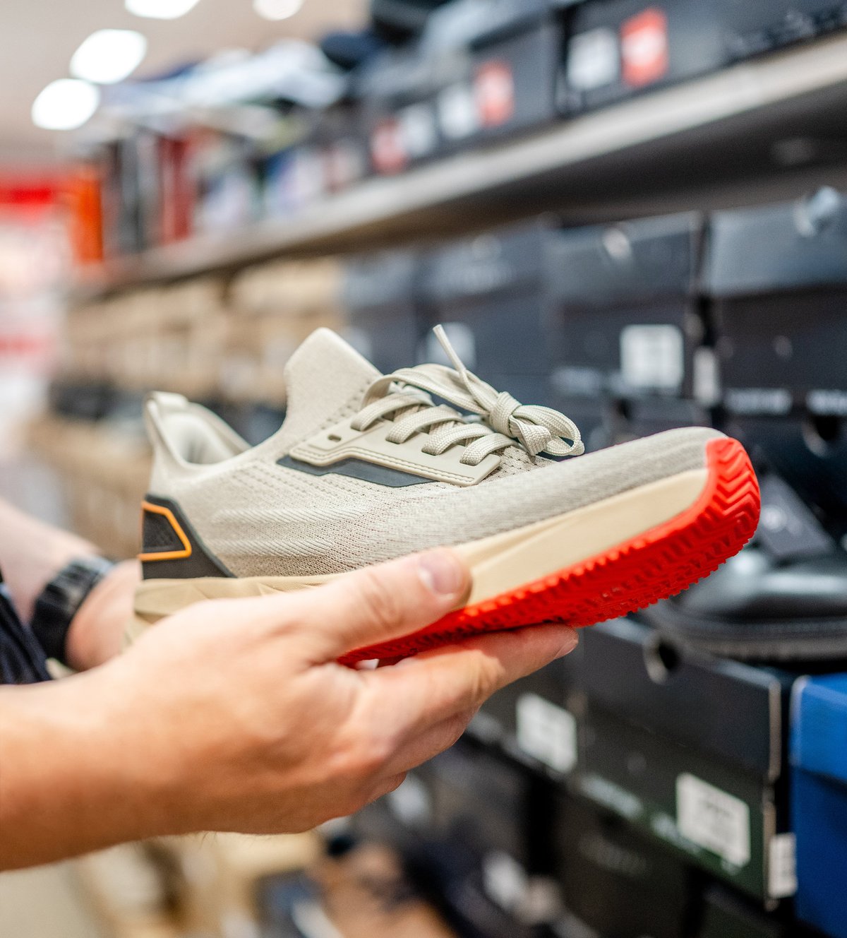 Hand holding a grey sports shoe with a red sole while shopping